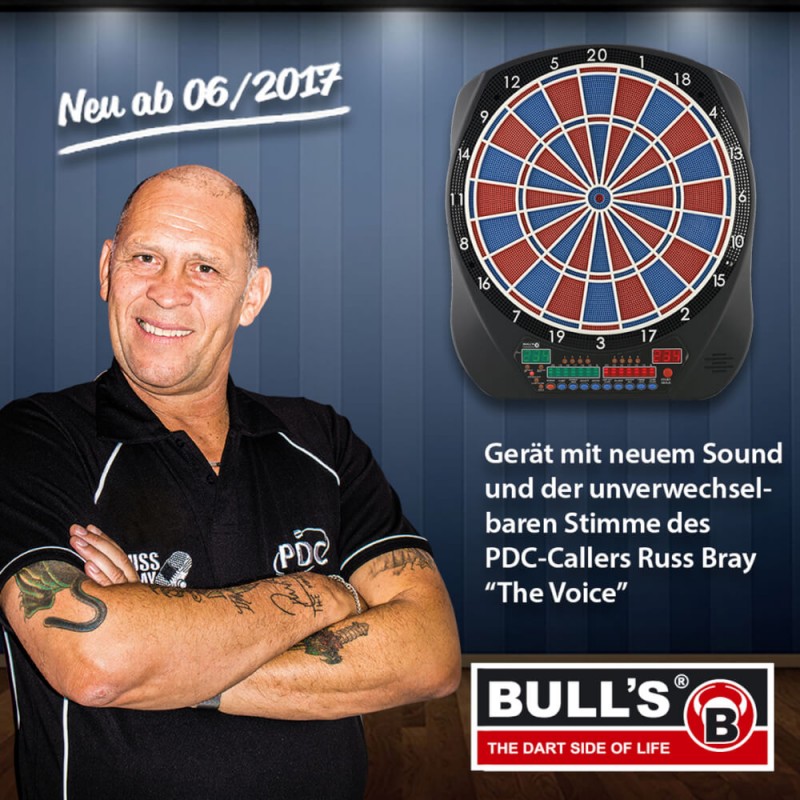 Mann steht lächelnd vor einer elektronischen Dartscheibe mit deutschem Text und Bull's-Logo.