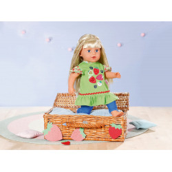 Eine blonde Puppe im grünen Kleid sitzt auf einem mit Erdbeeren verzierten Korb in einem pastellfarbenen Raum.